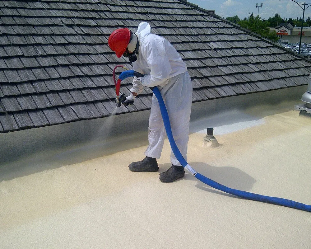 Worker spraying foam insulation onto a commercial flat roof beside a shingle-pitched roof in long island.